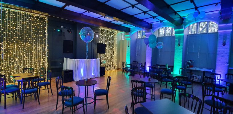 A function room lit up for a private event with uplighters and fairy light curtains.